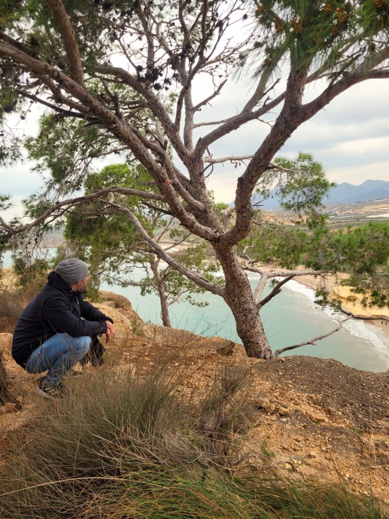 Mann sitzt in der Natur mit Blick auf Meer und Landschaft als Symbol für Reflexion und innere Orientierung